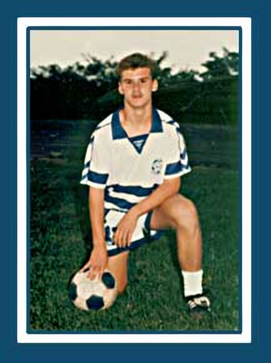 Scott Christian kneeling on the field with a soccer ball